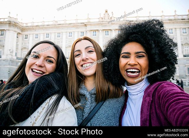 Cheerful female friends standing against Madrid Royal Palace, Spain