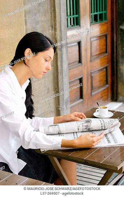 Young woman reading the newspaper at a sidewalk cafe