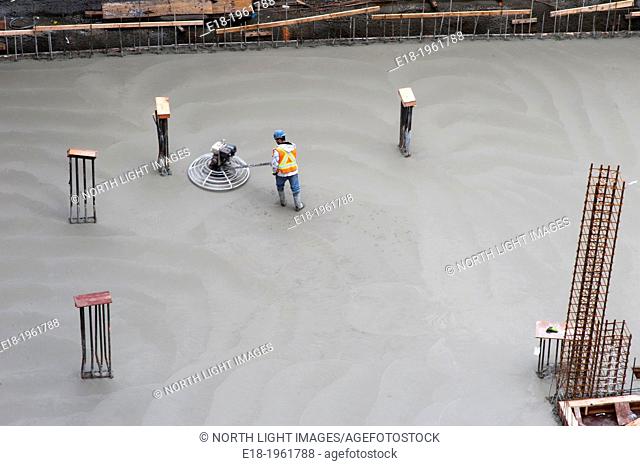 Canada, BC, Vancouver. Construction worker leveling concrete on floor our new building