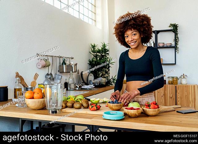 Happy young woman with fresh fruits at table in kitchen