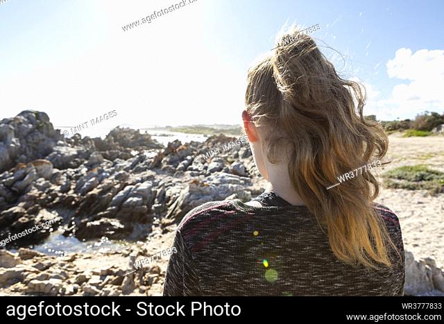 Teenage girl looking out over a beach and jagged rocks to the ocean