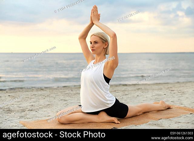 woman doing yoga pigeon pose on beach