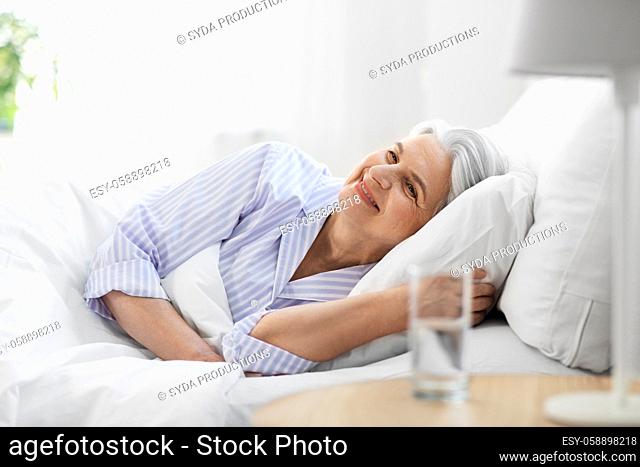 happy senior woman lying in bed at home bedroom