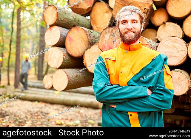 Junger Forstwirt vor einem Langholzwagen freut sich über die Holzernte