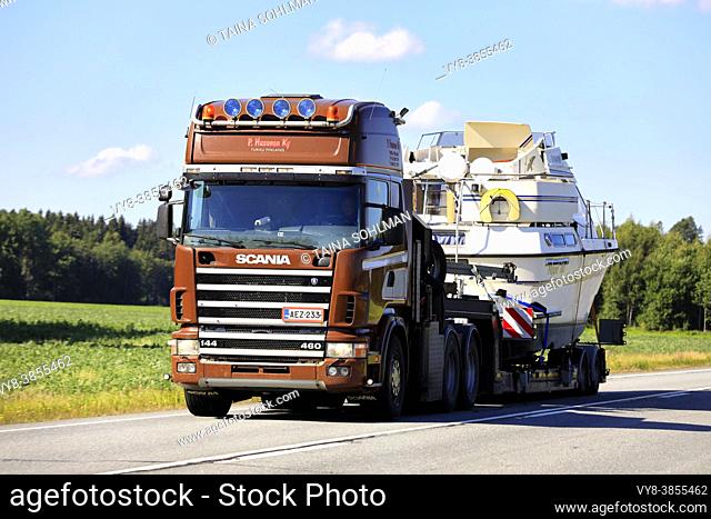 Brown Scania 144 460 semi trailer of P Husonen Ky transports recreational boat on highway 10 as oversize load. Tammela, Finland. August 21, 2020