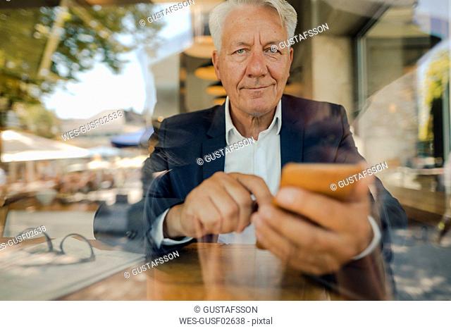 Portrait of senior businessman using cell phone in a cafe