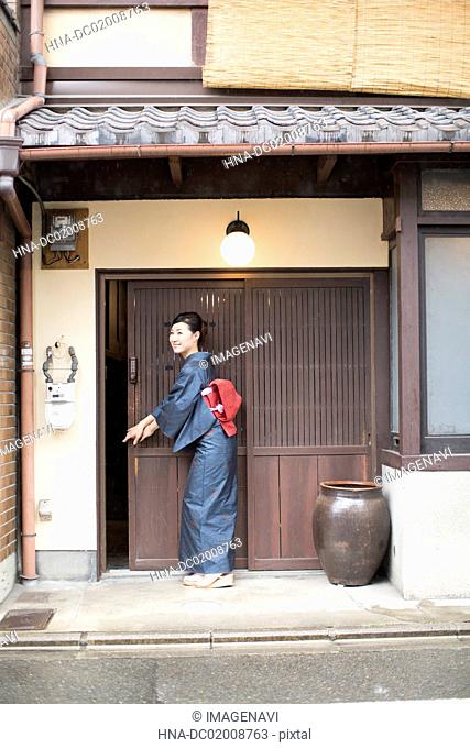 Mid Adult Japanese woman in kimono opening door