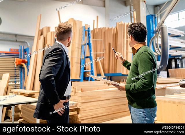 Two¶ÿcarpenters¶ÿtalking in front of stacked wood planks in production hall