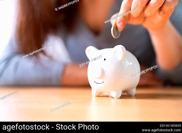 Woman's Hand Inserting Coin In Piggybank Over Wooden Desk