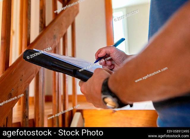A close up view on the hands of a professional building inspector, standing near a staircase filling in forms on overall environmental quality indoors