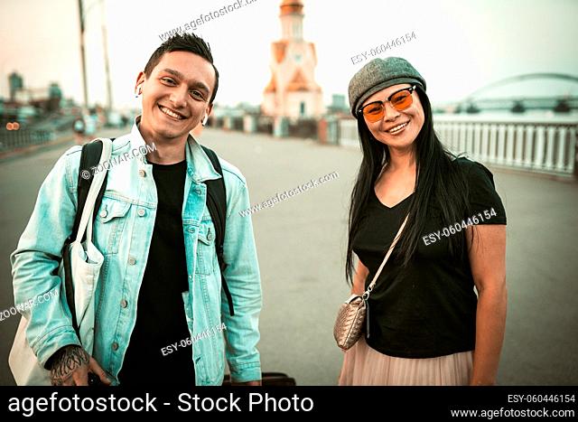 Two friendly travelers are toothy smiles looking at camera on background of the spacious city promenade. Travel concept