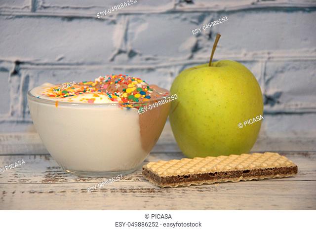Ice cream in a bowl decorated with sprinkling, green apple and waffle, lie on the table
