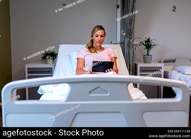 Caucasian female patient lying on hospital bed using digital tablet
