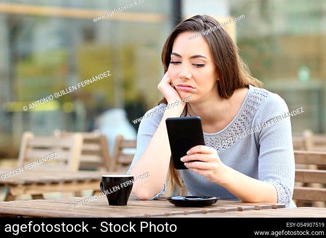 Bored girl looking disappointed at her smart phone on a cafe terrace