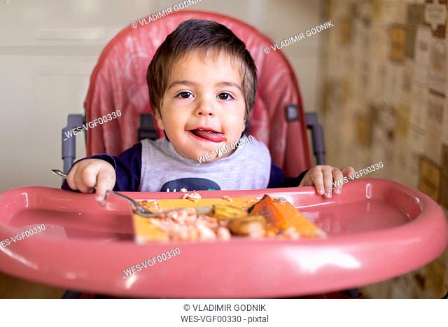 Portrait of little boy sitting on high chair eating vegetables