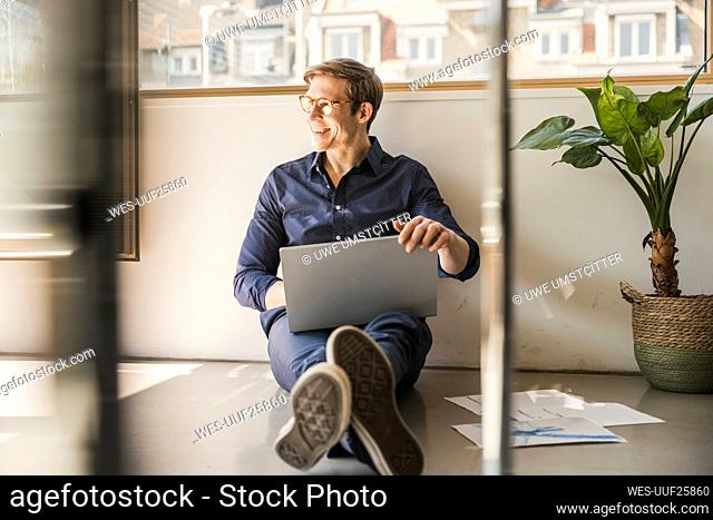 Businessman sitting on the floor in office using laptop