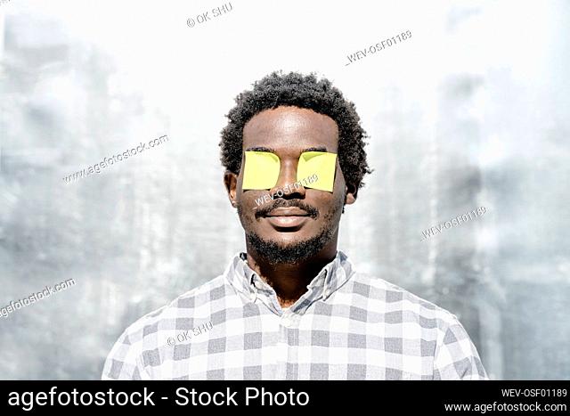 Man with adhesive notes over eyes in front of wall