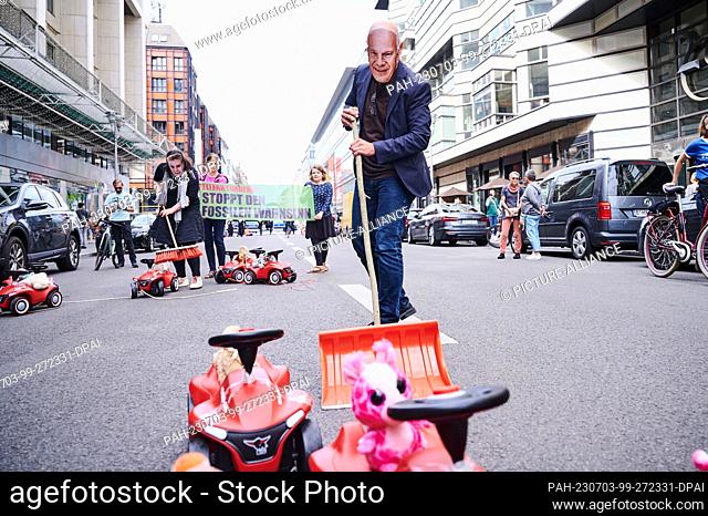 dpatop - 03 July 2023, Berlin: A demonstrator wearing a ""Kai Wegner mask"" symbolically sweeps the Bobby Cars out of the way on Friedrichstraße