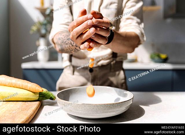 Man putting chopped vegetable in bowl at kitchen