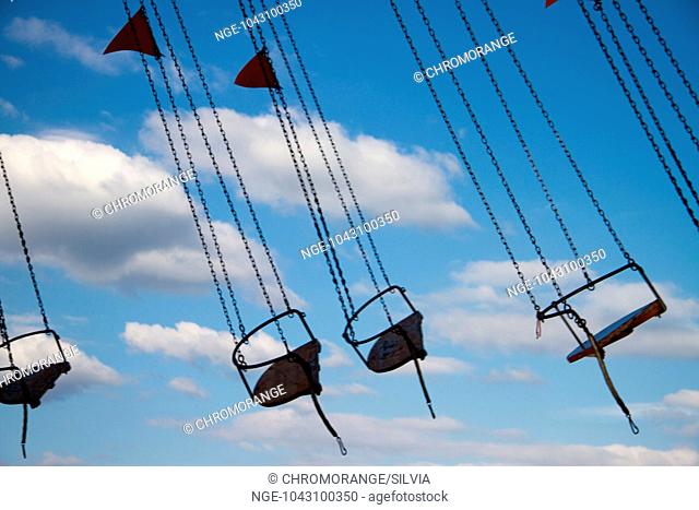 empty seats of a chairoplane in movement in front of blue sky with clouds