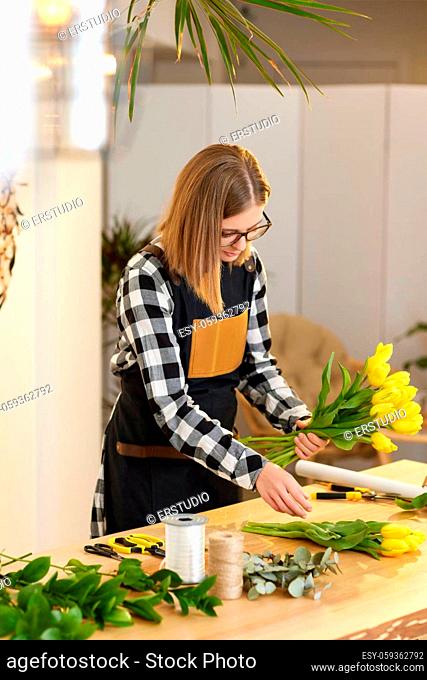 Florist woman makes a bouquet of fresh yellow tulips. Floral design studio