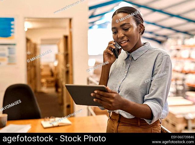 Smiling young African female manager standing in a large textile warehouse talking on the phone and using a table