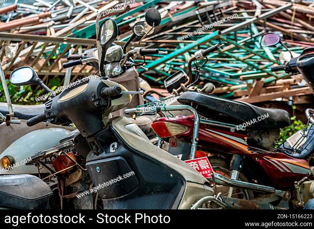 Yangshuo, China - August 2019 : Used, old, damaged and disposed of motorbikes, motorcycles and scooters piled up in the yard outside metal recycling plant in...