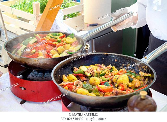 Cheff cooking traditional Mediterranean octopus with potatoes and vegetable on street stall on international street food festival of Odprta kuhna