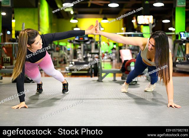 Two sporty women doing high five while workout push up exercise in Gym. High quality photo