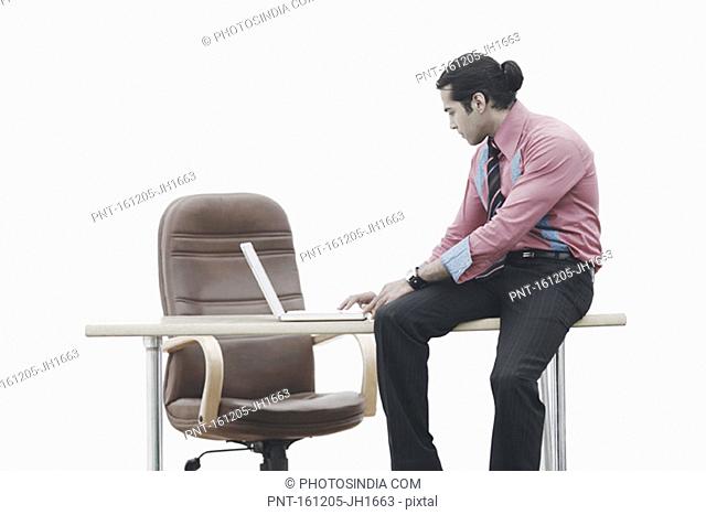 Side profile of a businessman sitting on a table working on a laptop