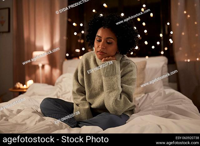 sad woman in sweater on bed at home at night