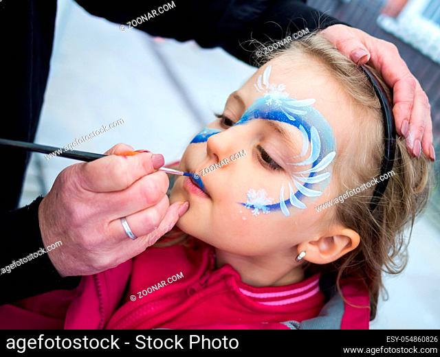 Little girl having her face painted during party by an artist
