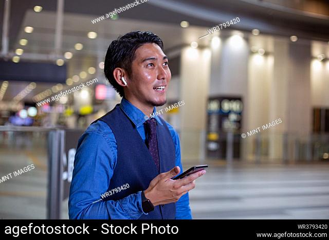 A young businessman in the city, standing looking around, holding his mobile phone