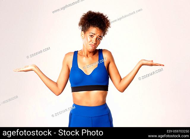 Concept of sport and workout. Studio shot of clueless and confused african-american female athlete, shrugging and sulking
