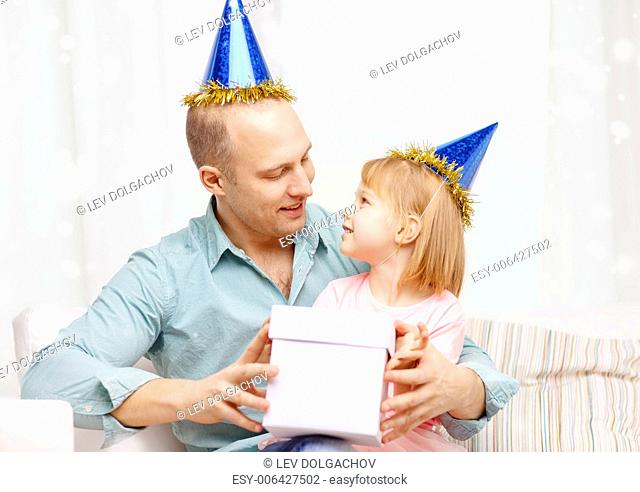 family, children, celebration, holidays and happy people concept - happy father and daughter in party caps with gift box