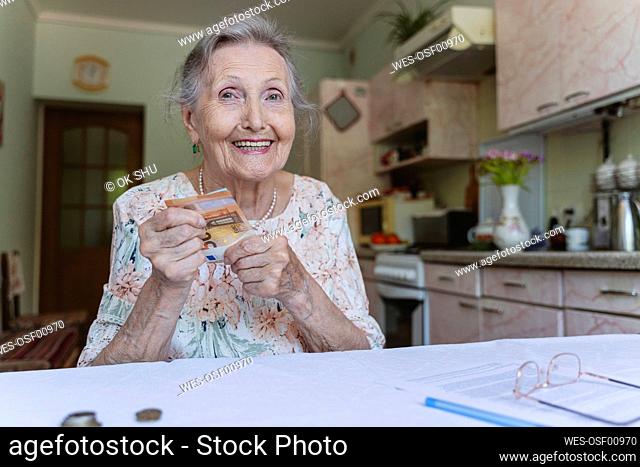 Happy senior woman with savings money at home