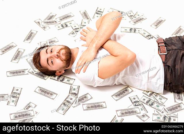 young handsome happy man with a beard in a white shirt lying on hundred dollar bills. lottery winner