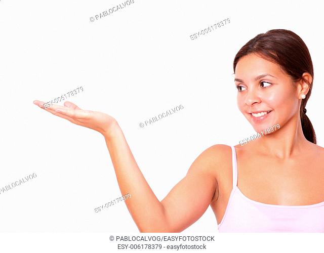 Portrait of pretty hispanic lady on pink t-shirt holding her right palm up while smiling and looking to her right on isolated white background - copy space