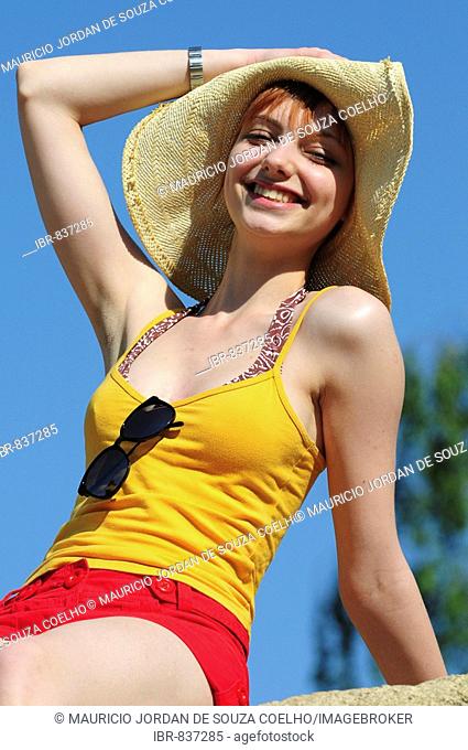 Red-haired woman wearing a yellow top, sun hat, sitting on a rock, summer, attractive, smiling
