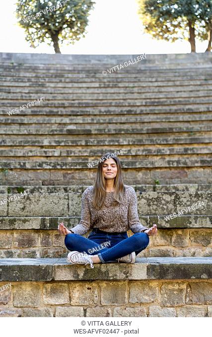 Young woman sitting outdoors on stairs doing yoga