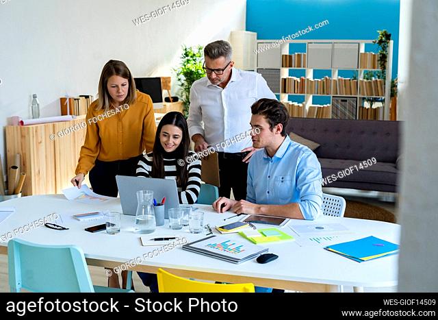 Young businesswoman with colleagues watching laptop at desk in office