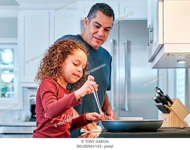 Father helping daughter cook on hob in kitchen
