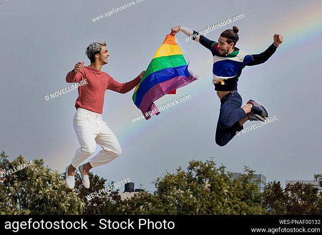 Smiling men with scarf jumping against rainbow in clear sky