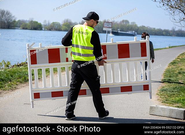 04 April 2020, Hessen, Eltville: A security officer sets up a barricade barricade on the banks of the Rhine. Some paths along the Rhine are closed to cyclists...