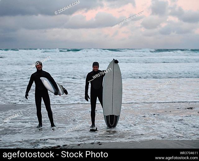 Authentic local Arctic surfers going by snowy beach after surfing in Northern sea. Norwegian sea coastline. Winter water activities extreme sport