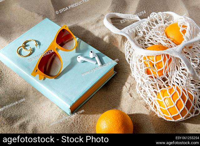 bag of oranges, earbuds and sunglasses on beach