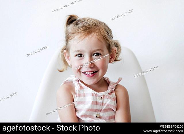 Happy blond girl sitting on chair against white background