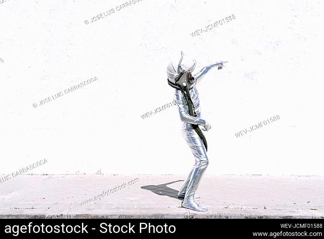 Boy in astronaut costume pointing at wall while standing on sidewalk in city