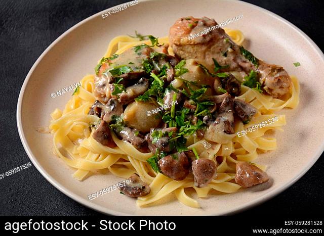 Fricassee - French Cuisine. Chicken stewed in a creamy sauce with mushrooms in a white plate on a black table