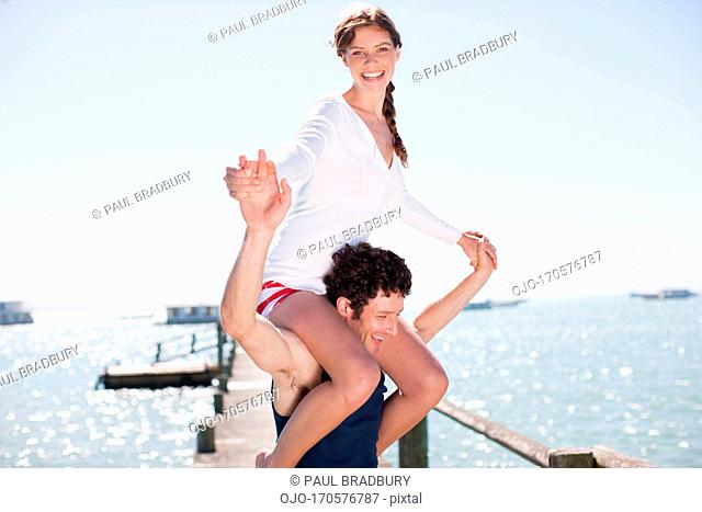 Man carrying wife on shoulders on pier at ocean